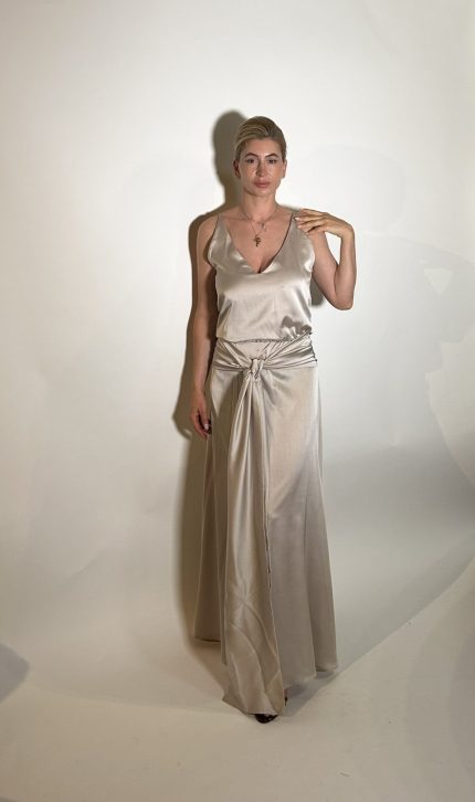 Vestito raso elasticizzato liscio argento. Presenta uno scollo ampio a V davanti e uno scollo tondo dietro con elastico in vita, da dietro una fascia che si raccoglie sul davanti e sui fianchi con un nodo che scende in giu che aggiunge liberta di movimento e un tocco moderno. Misure taglia M Spalle 36 cm Seno 92 cm Giro vita 48cm Fianchi 100cm Lunghezza vestito 150 cm