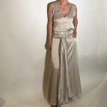 Vestito raso elasticizzato liscio argento. Presenta uno scollo ampio a V davanti e uno scollo tondo dietro con elastico in vita, da dietro una fascia che si raccoglie sul davanti e sui fianchi con un nodo che scende in giu che aggiunge liberta di movimento e un tocco moderno. Misure taglia M Spalle 36 cm Seno 92 cm Giro vita 48cm Fianchi 100cm Lunghezza vestito 150 cm