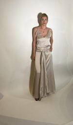 Vestito raso elasticizzato liscio argento. Presenta uno scollo ampio a V davanti e uno scollo tondo dietro con elastico in vita, da dietro una fascia che si raccoglie sul davanti e sui fianchi con un nodo che scende in giu che aggiunge liberta di movimento e un tocco moderno. Misure taglia M Spalle 36 cm Seno 92 cm Giro vita 48cm Fianchi 100cm Lunghezza vestito 150 cm